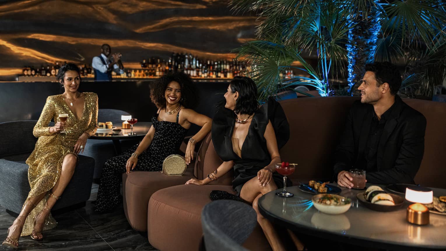 Three women and one man mingle over cocktails at Dubai hotel rooftop lounge