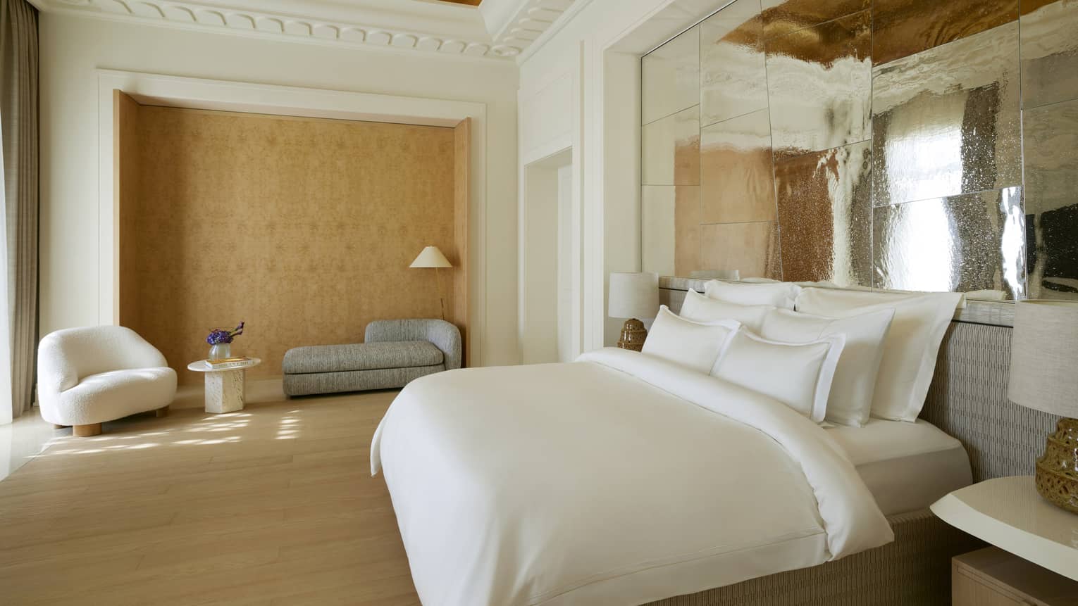 Primary bedroom of a luxury hotel suite, with king bed under an intricate painting ceiling with crown molding