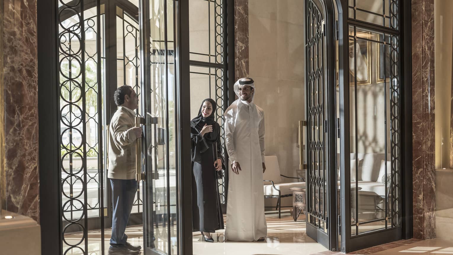 A man in a Four Seasons uniform opens the wrought iron doors for a couple. 