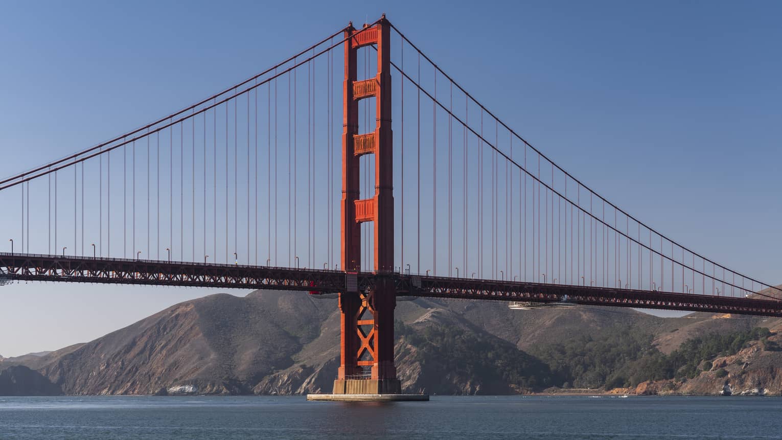 A red metal bridge with a large landmass of hills and mountains behind it.