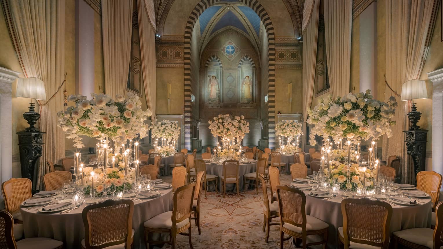 Grand dining room with tall arched ceilings and round elegantly set tables with tall white flower centrepieces