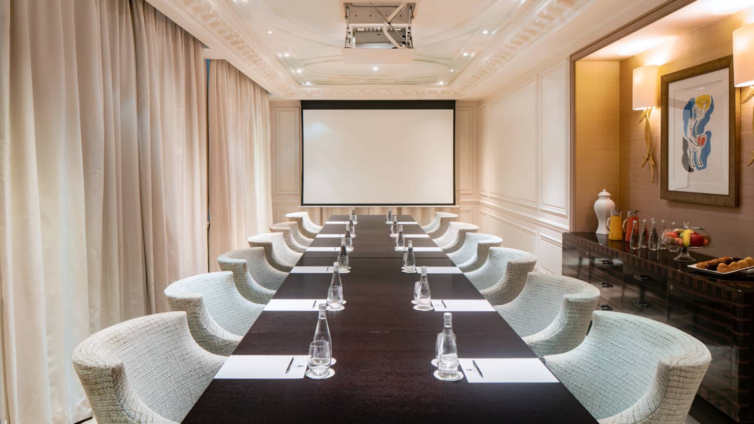 Long, narrow meeting room with conference table and beige chairs, curtained window to left, rear screen