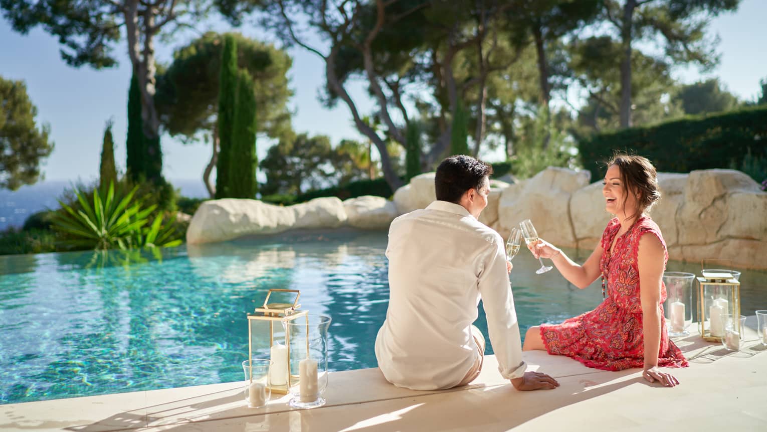 A couple toasts champagne while sitting at an outdoor pool