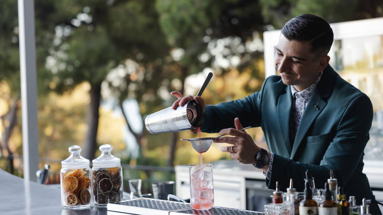 A bartender pours a pink beverage through a strainer into a glass with ice