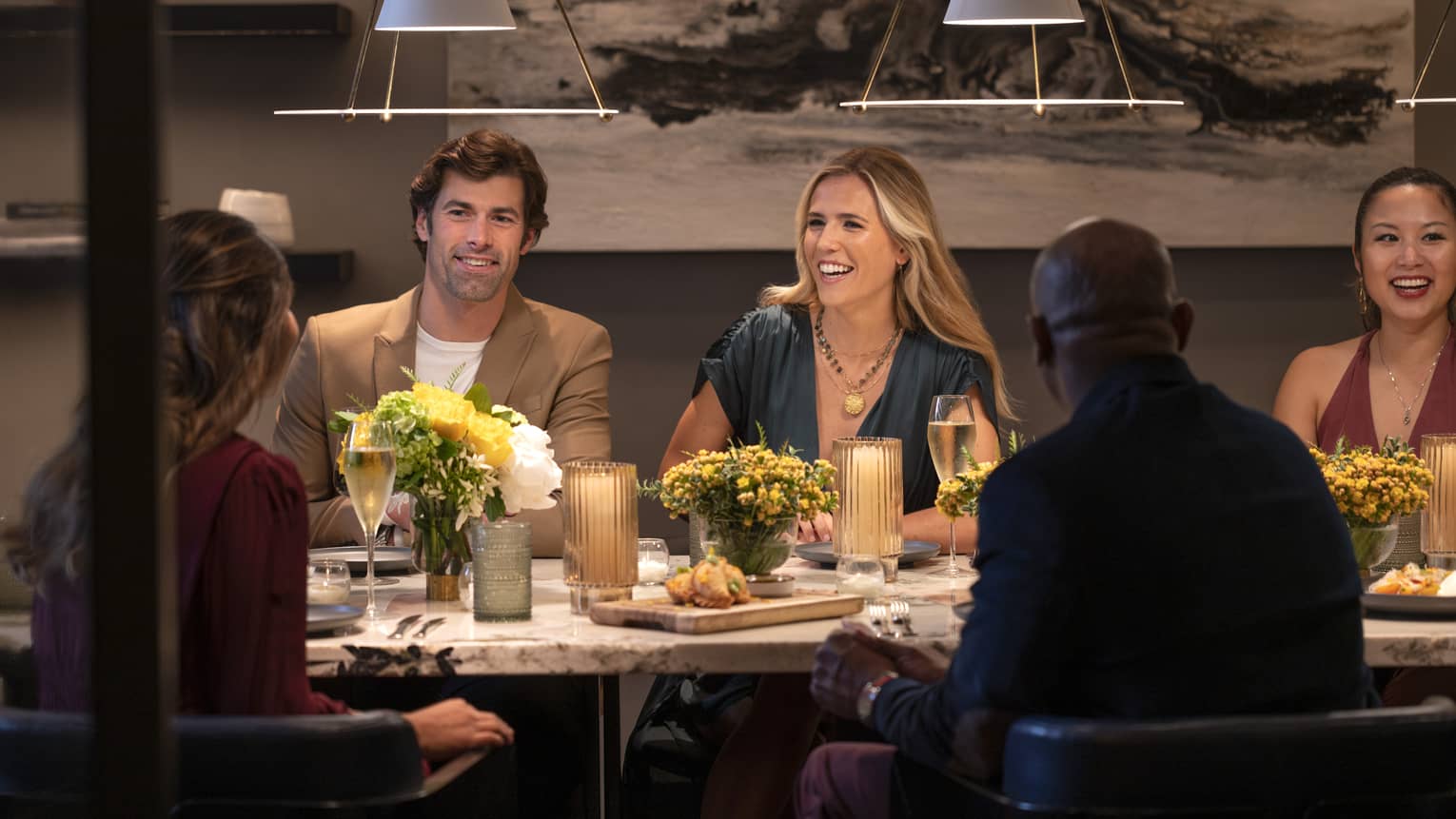 Guests sitting at a table and smiling at each other at a restaurant with overhead lighting