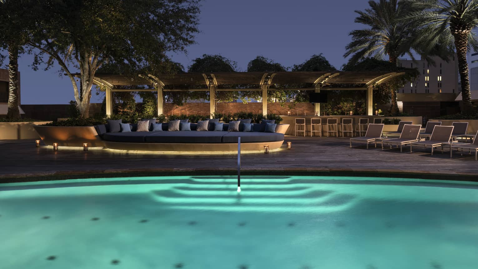 Outdoor swimming pool with lights and patio with large banquette at night