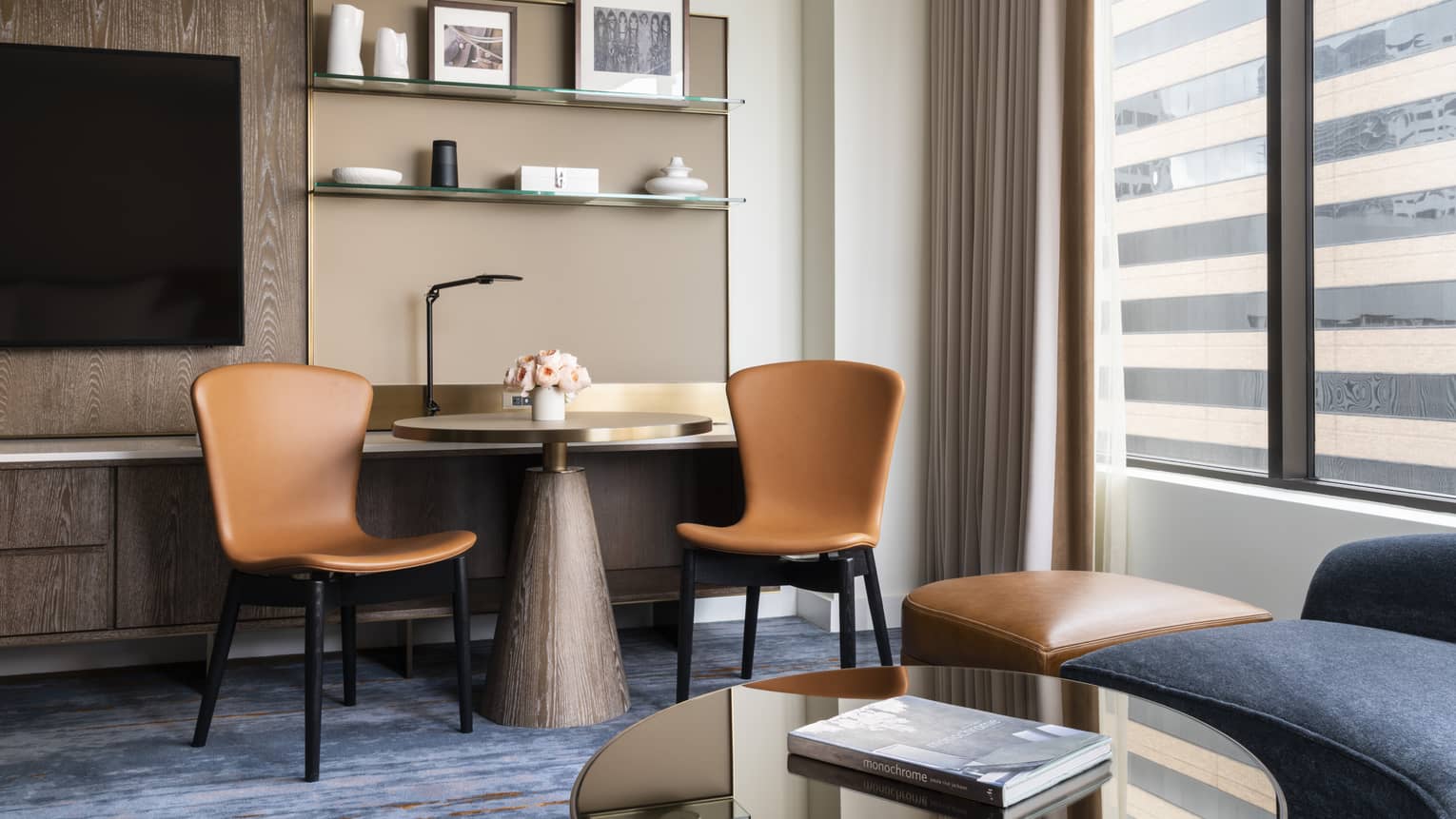 Round modern table with two light leather chairs, shelving, TV, window