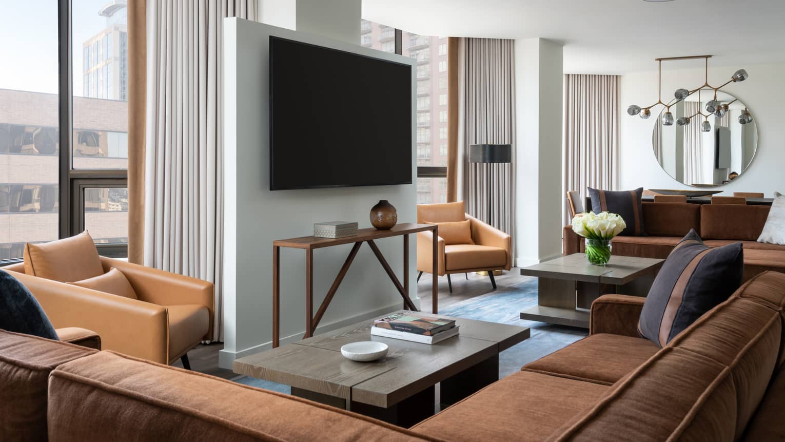 Living room with brown suede sectional sofa, light brown leather arm chairs, coffee table, hanging TV, windows