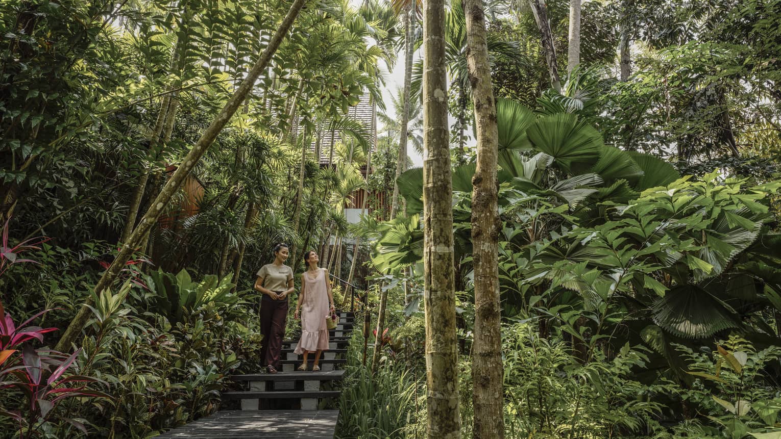 Female guest and spa staff member walk along foliage-lined pathway to the spa