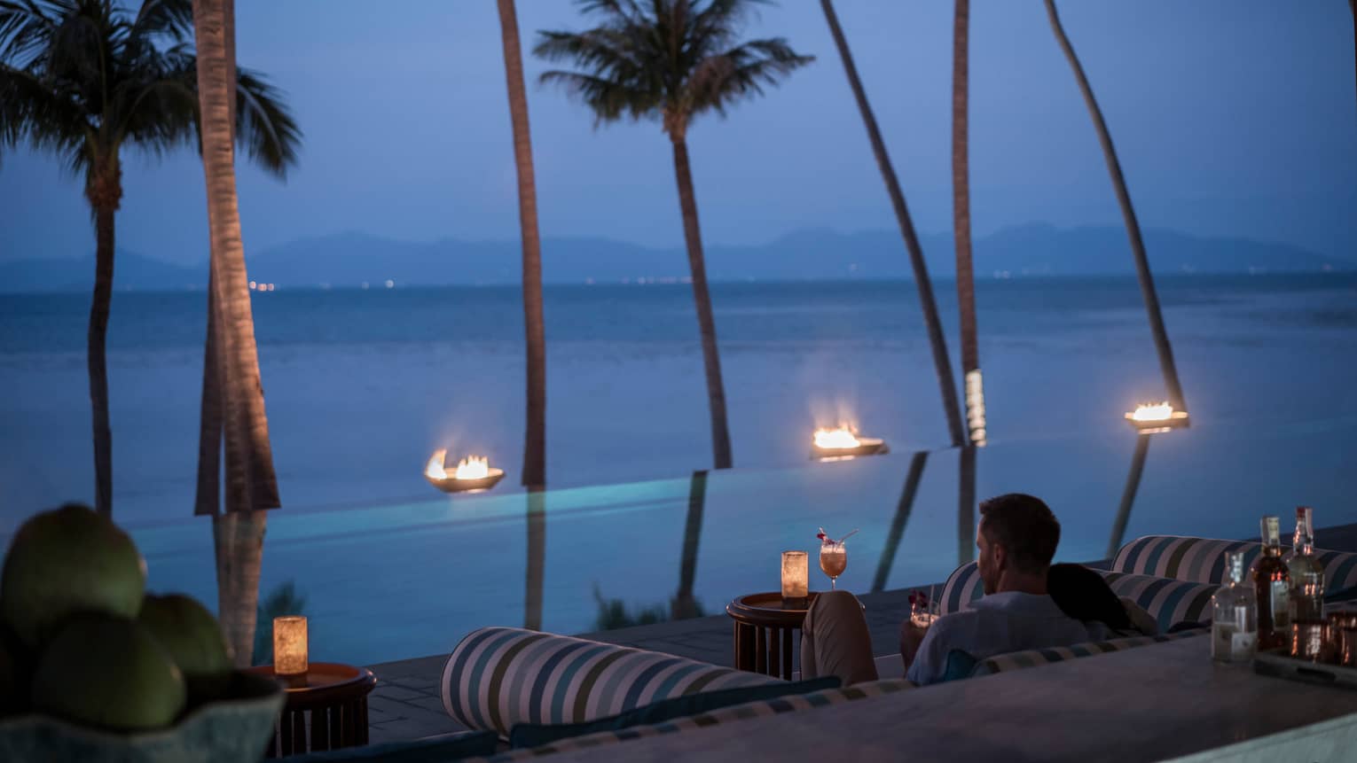 Guests sit outside CoCoRum enjoying drinks by the infinity pool with views of the Gulf of Thailand