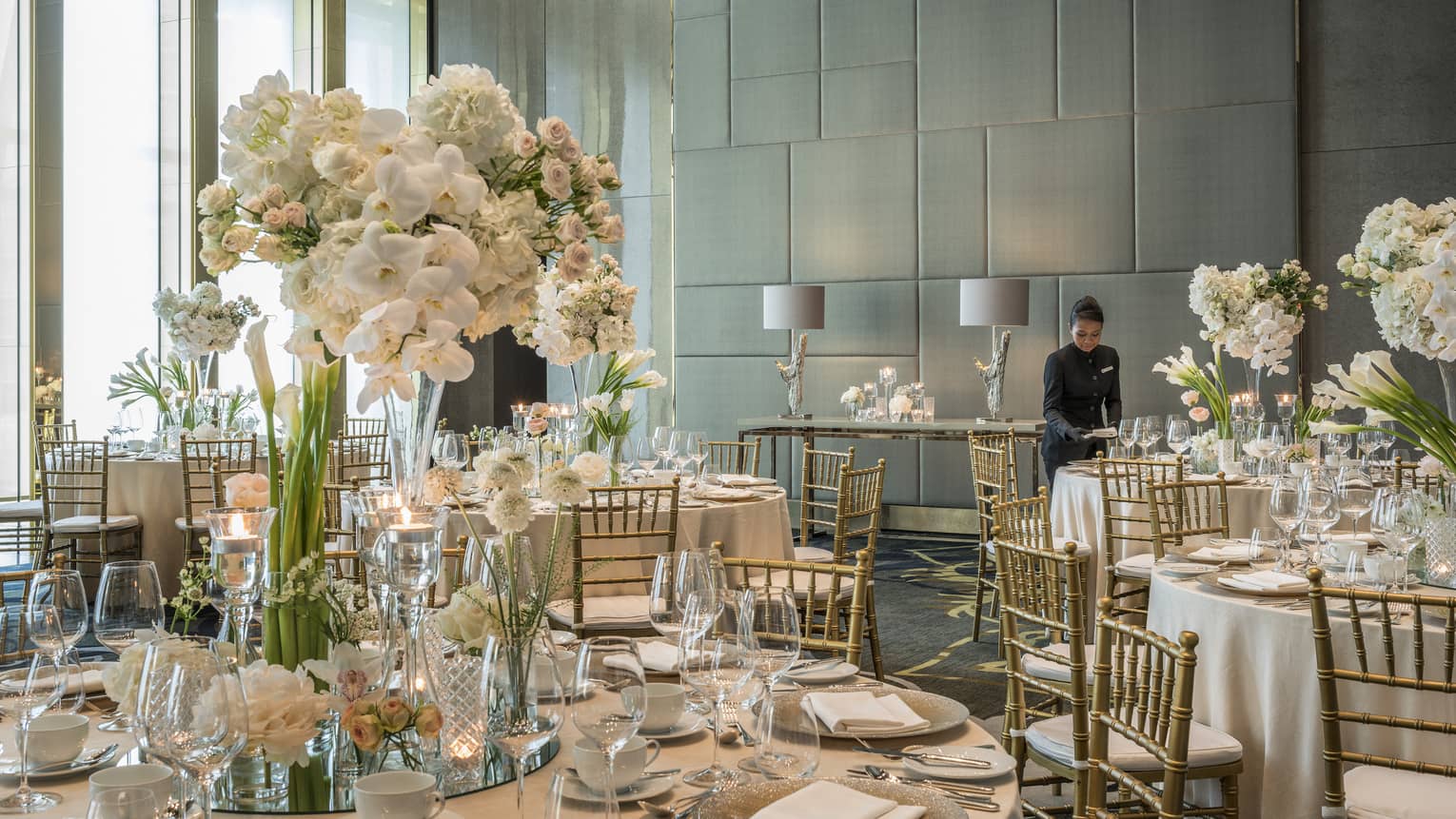 Hotel staff sets table in Western Banquet room with round tables, white flowers 