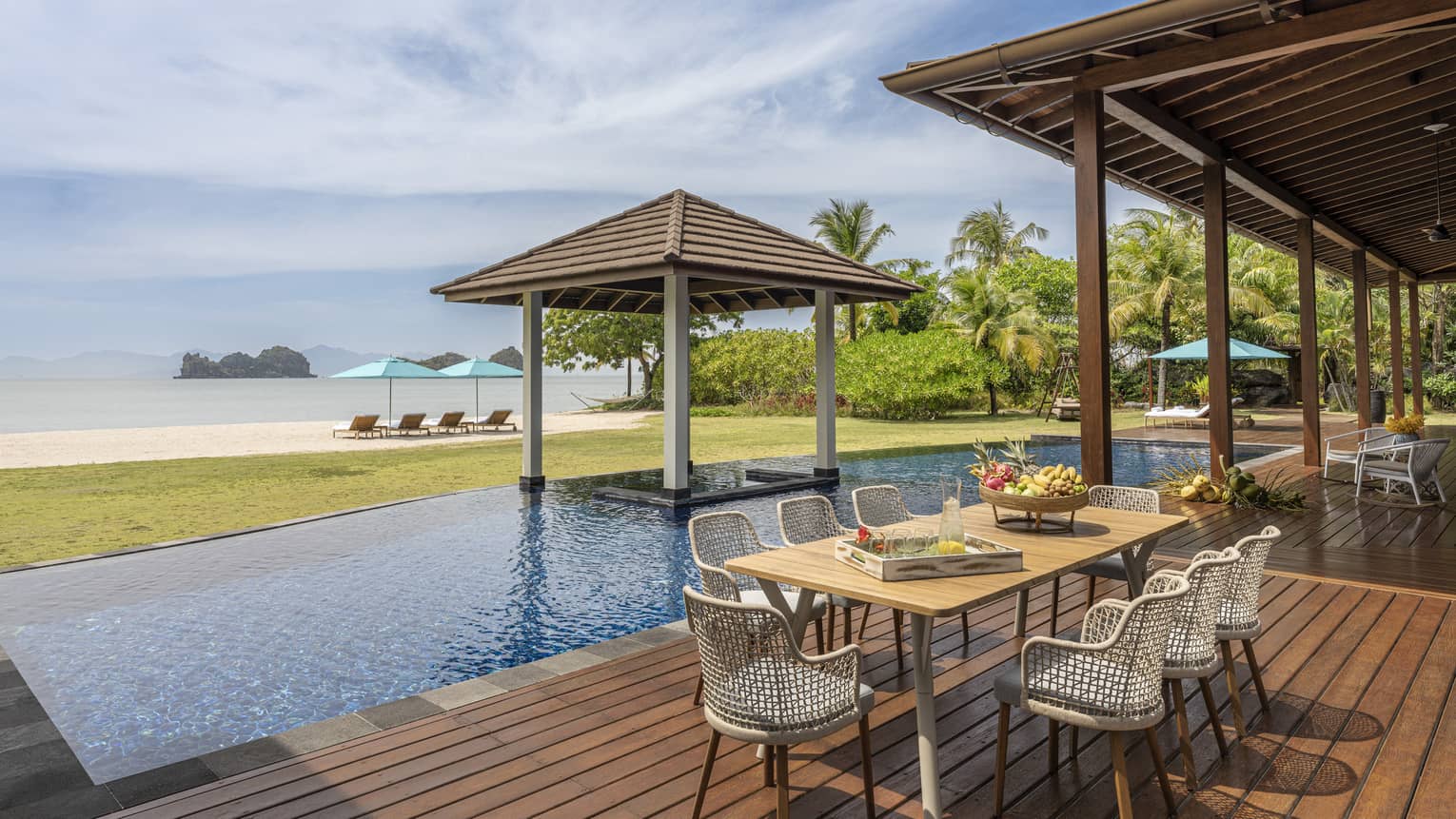 Pool deck with dining table, pool, covered lounge area and beach view