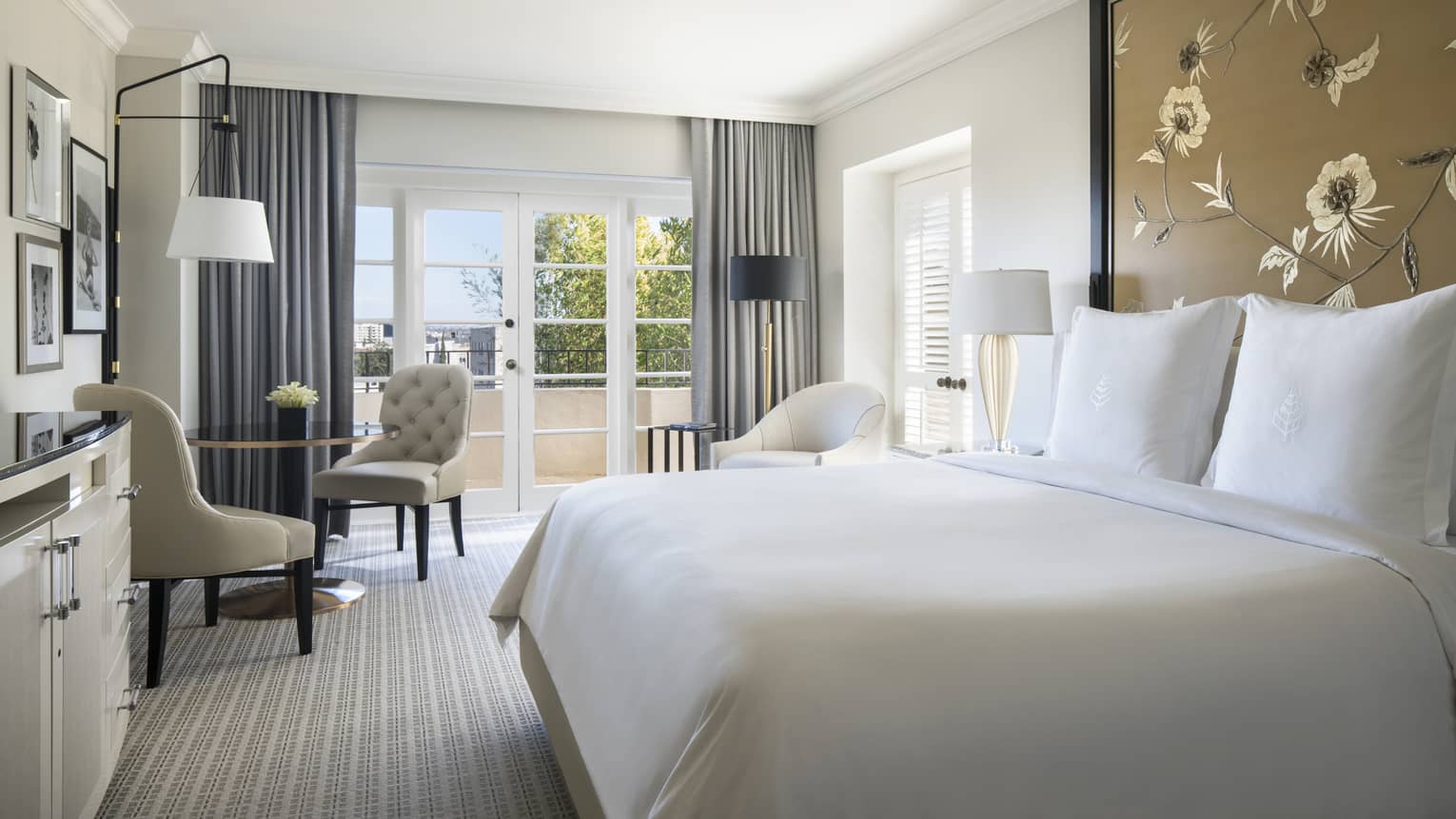 Premier Balcony Room bed with white linens against tall floral headboard, cafe table by balcony doors