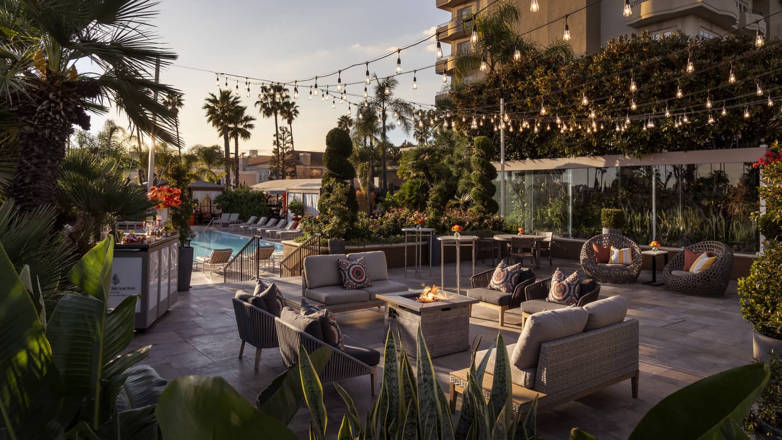 An outdoor seating area with fairy lights next to a pool and palm trees.