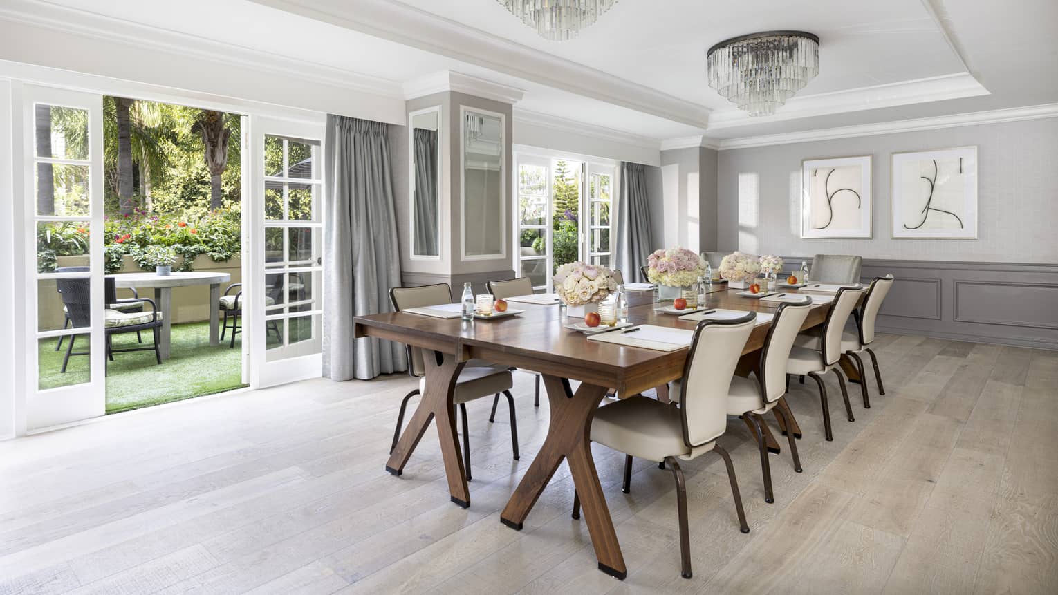 A meeting room with long wooden table, beige chairs and open patio doors.
