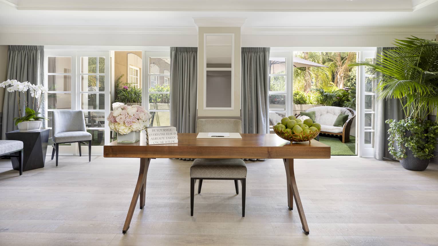 A desk in a room with plants and open patio doors leading outside.
