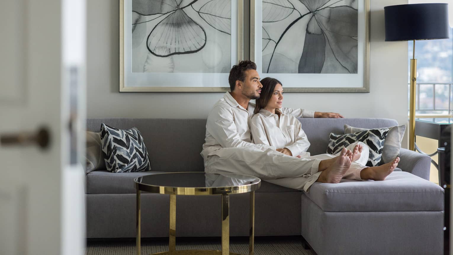 Two guests sitting on a couch in a living room with paintings on the wall behind them