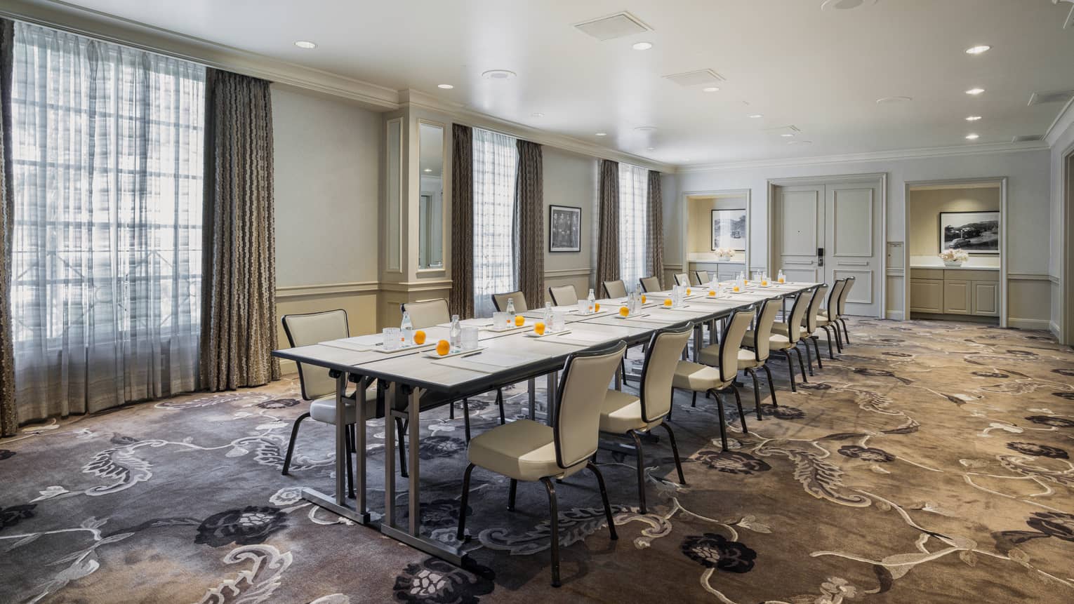 Meeting room set up boardroom style with floor-to-ceiling windows, ambient lighting and dark patterned carpet