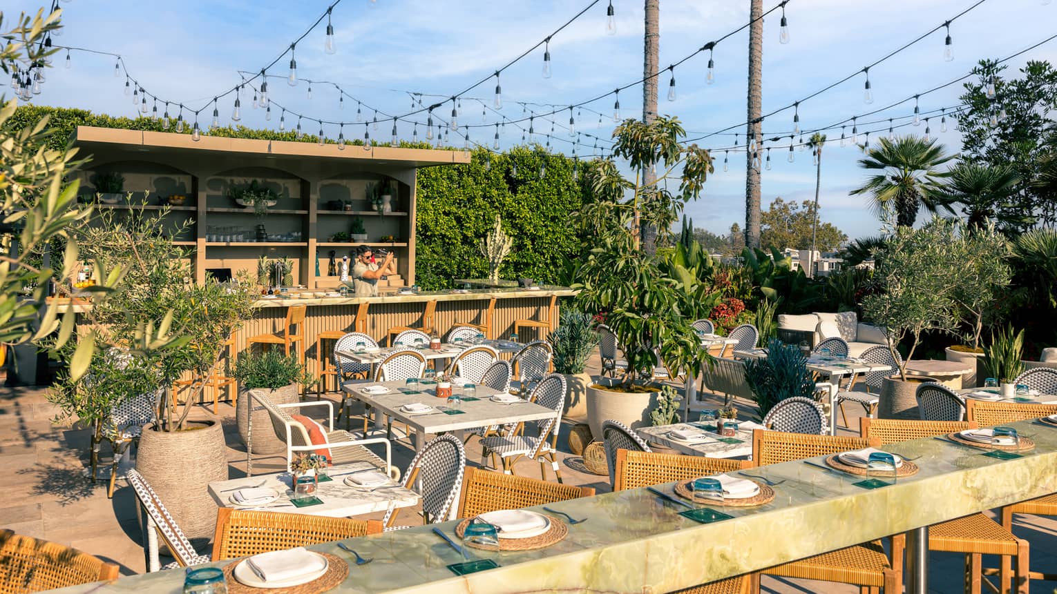 Outdoor restaurant with marble counter seating, various tables and a wooden bar area, all with rows of string lights overhead