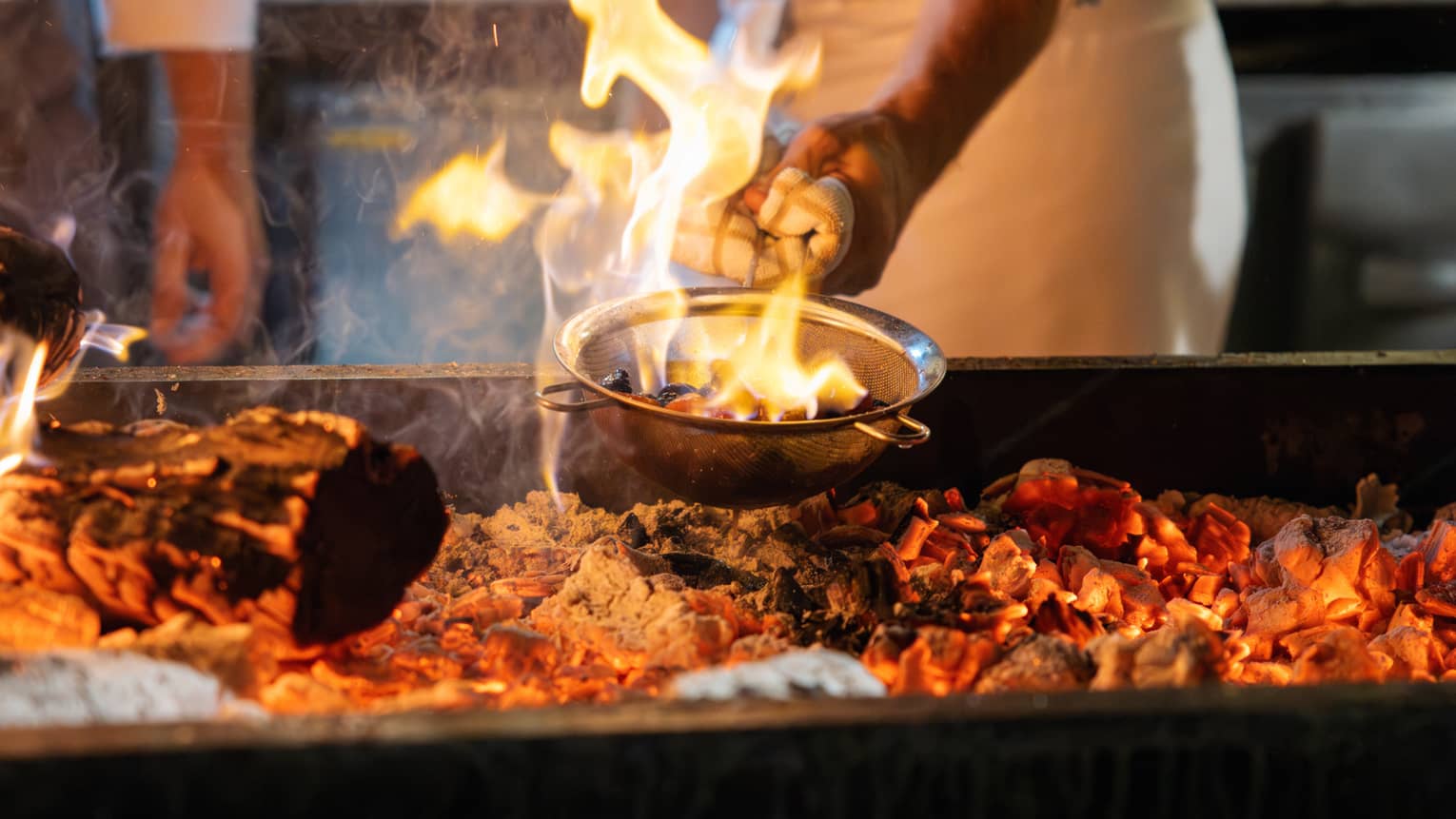 Chef cooking a dish over a fire grill.