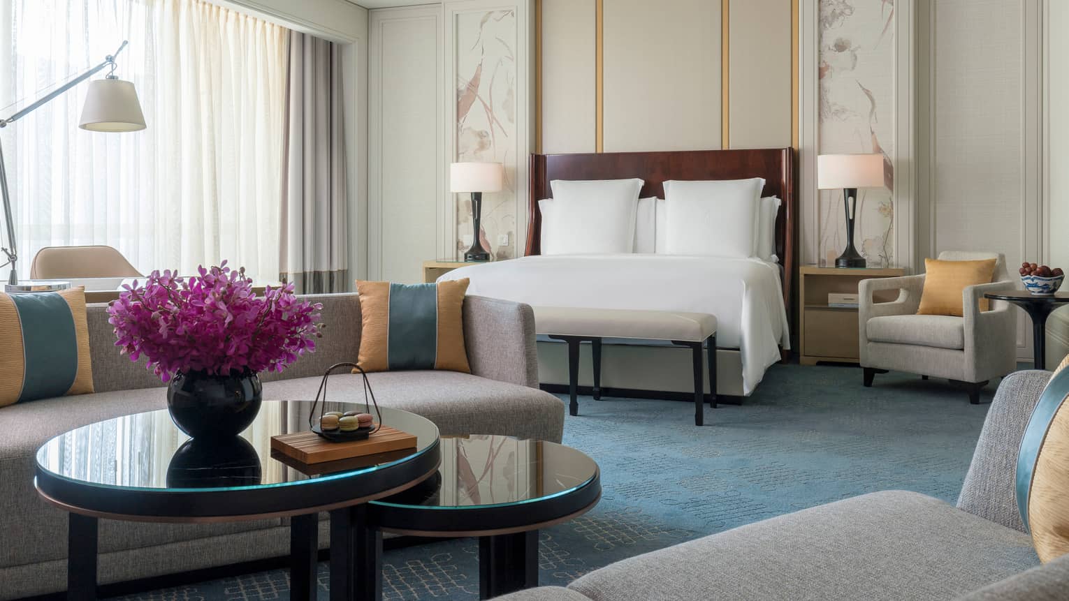 Junior Suite bed in front of grey sofa, coffee table with vase, purple flowers