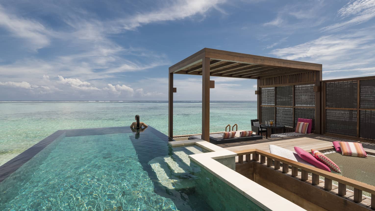 Woman looks out at ocean from private pool on sunny patio of sunset water villa