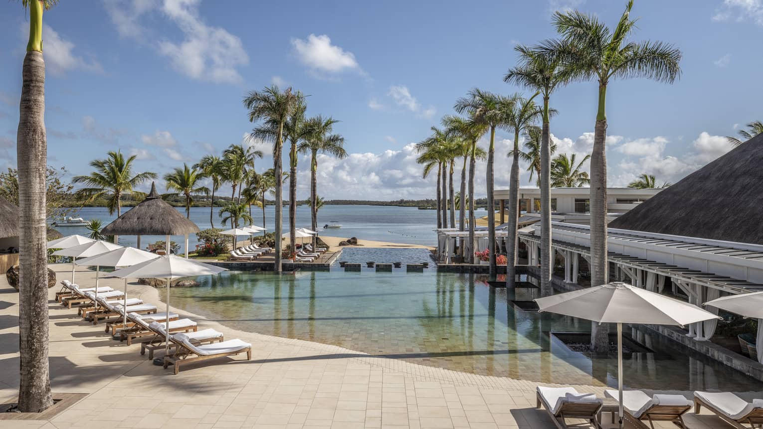 Wading pool with rows of lounge chairs and white umbrellas, flanked by palm trees