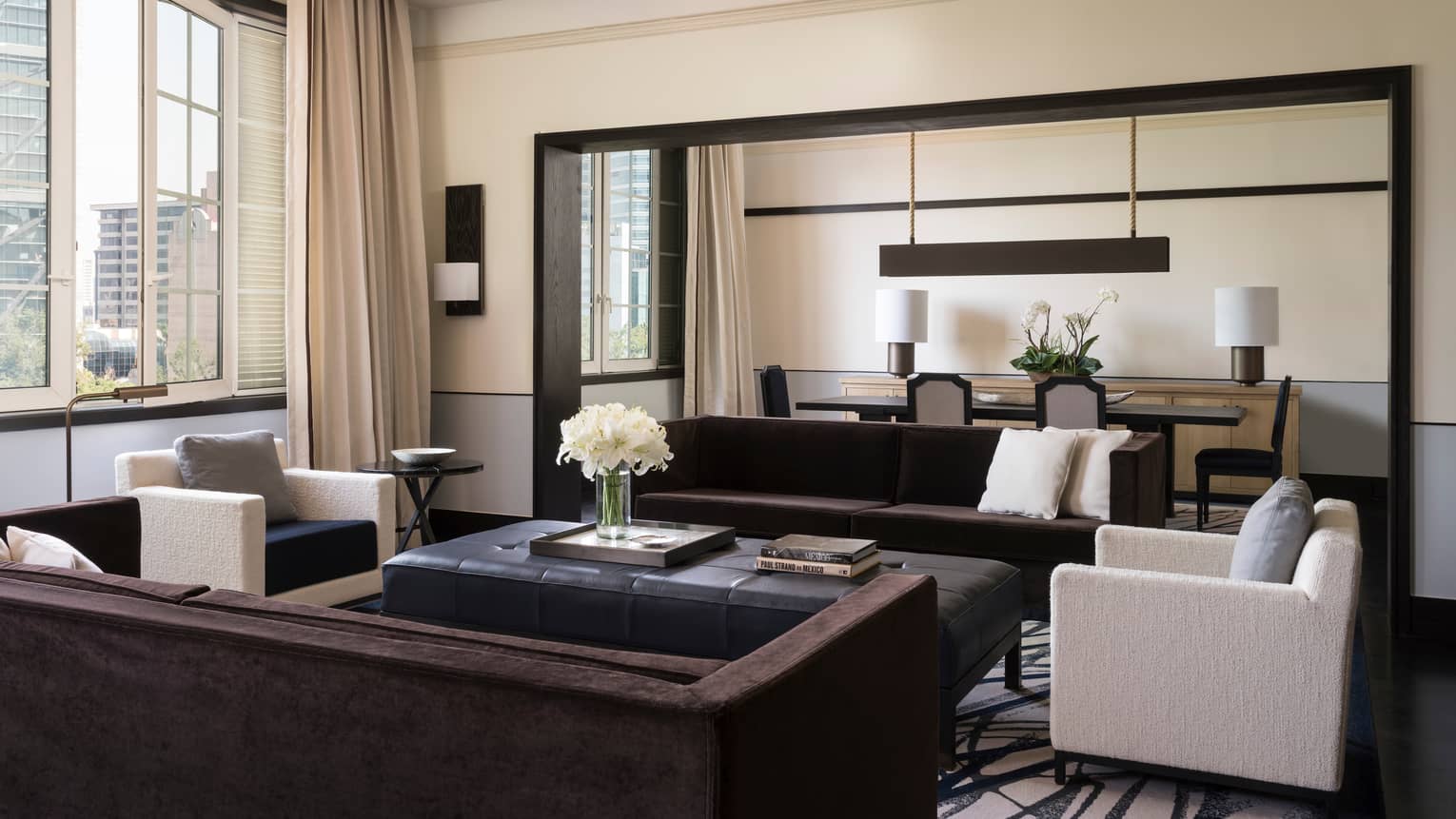 Presidential Suite bright living room with long sofas, white armchairs, tall sunny window, dining room