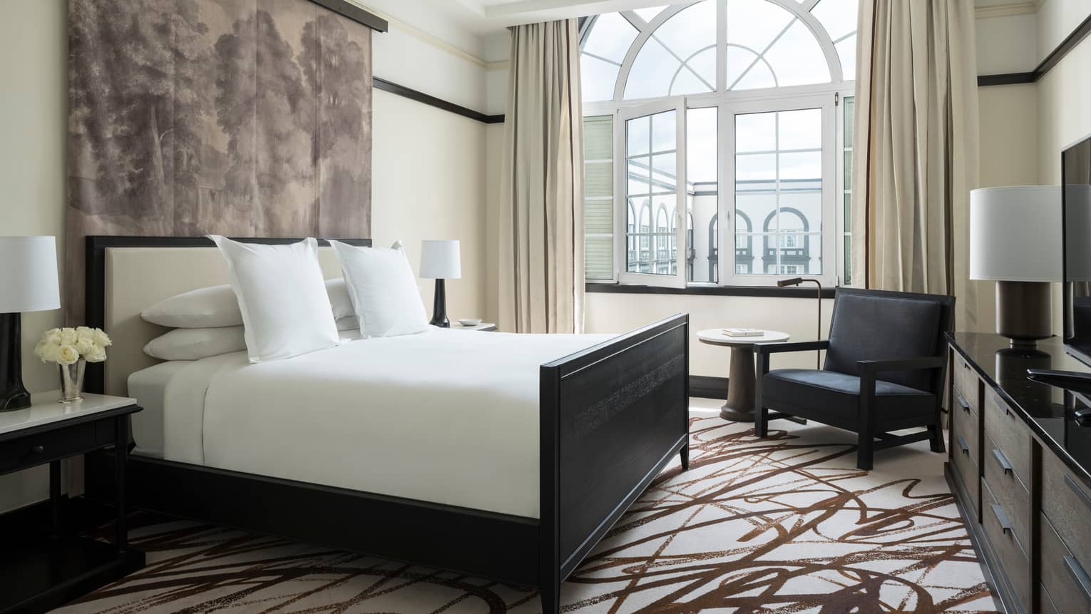 Ambassador Suite bed under print textile, black armchair under oversized arched window