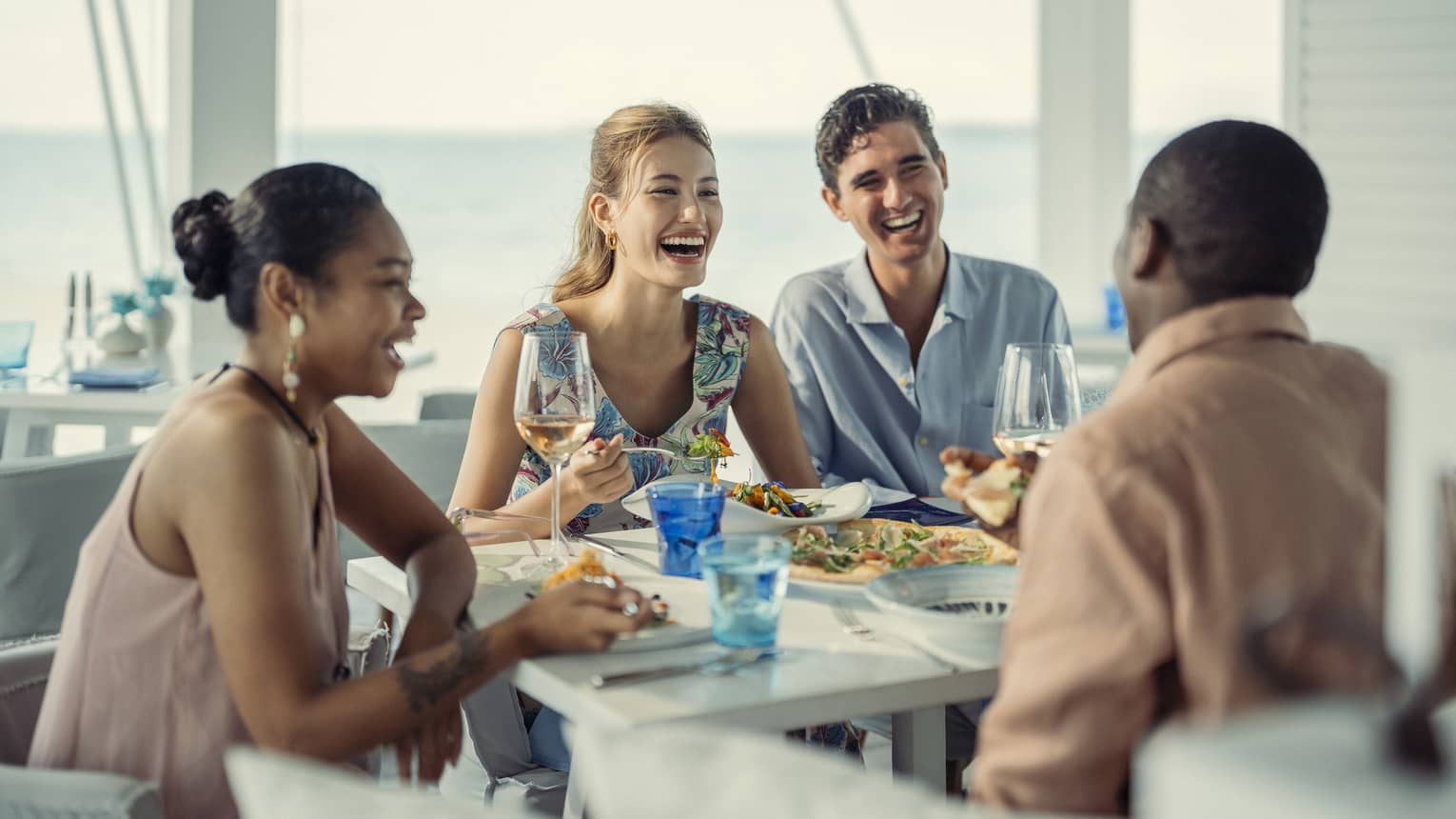 Two couples laugh as they share a meal at Blu Beach Club