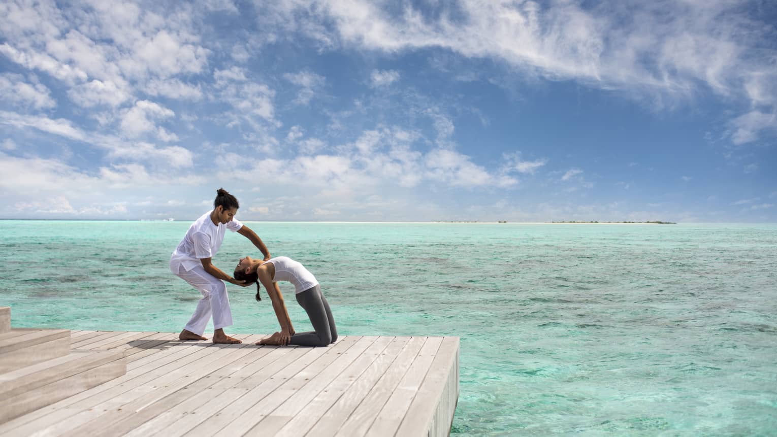 Woman leans back into hands of Yoga Therapist on dock over lagoon
