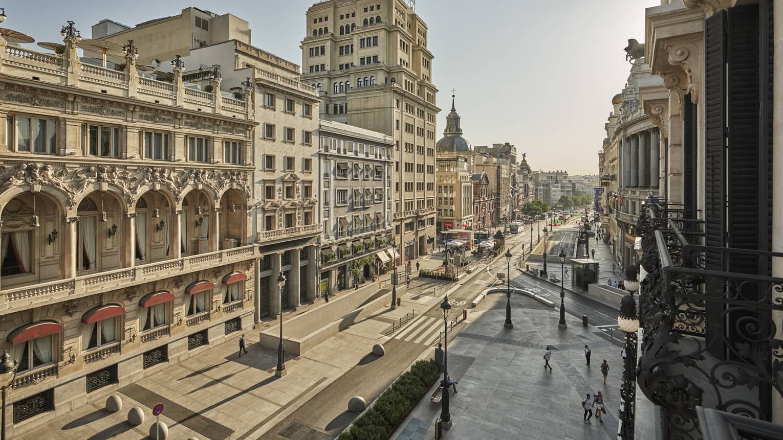 Street view from a Juliet balcony with historic buildings, arched windows and a mix of architectural styles lining a broad avenue on a clear day