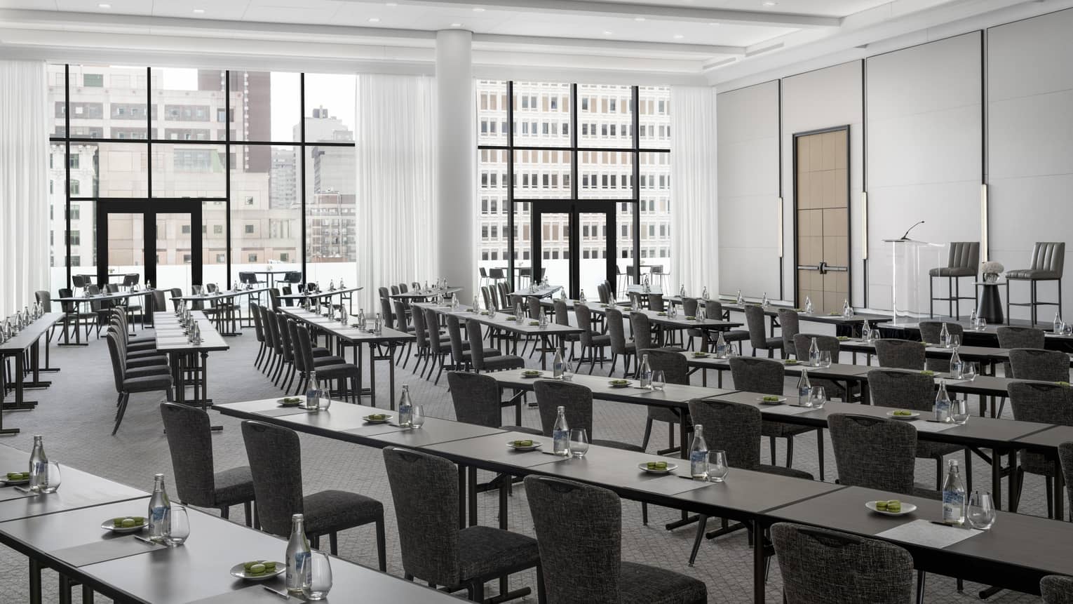 Rows of black tables set with green macaroons, water facing podium in light-filled ballroom