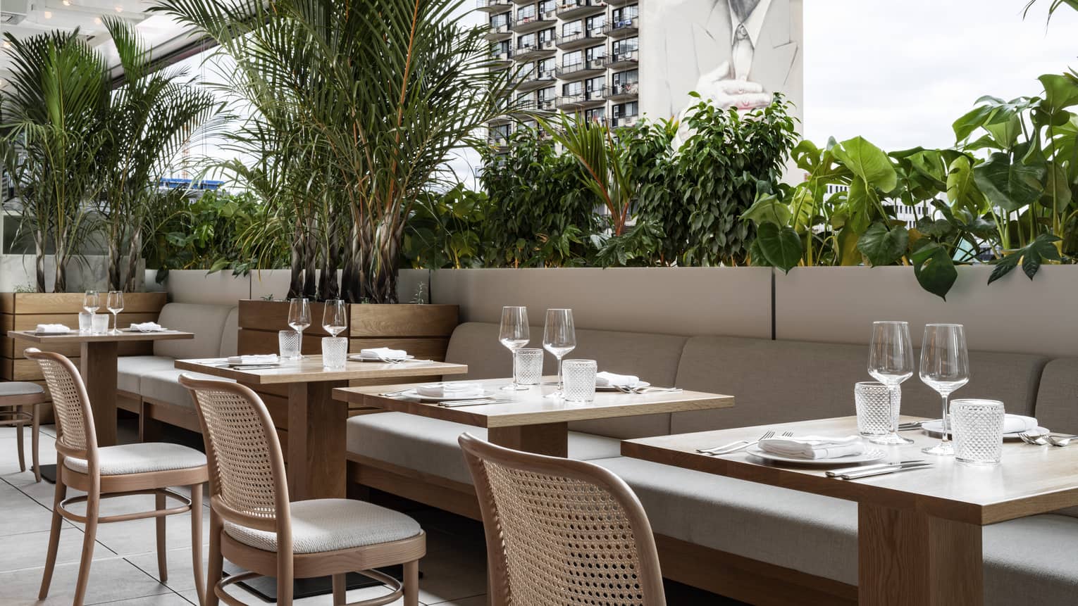 Terrace with banquets, tables set for dinner, greenery, overlooking building with graffitied image of Lennon Cohen 