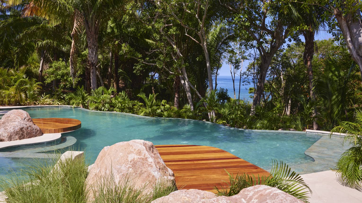 Pool surrounded by tropical forest, with the ocean visible through the trees