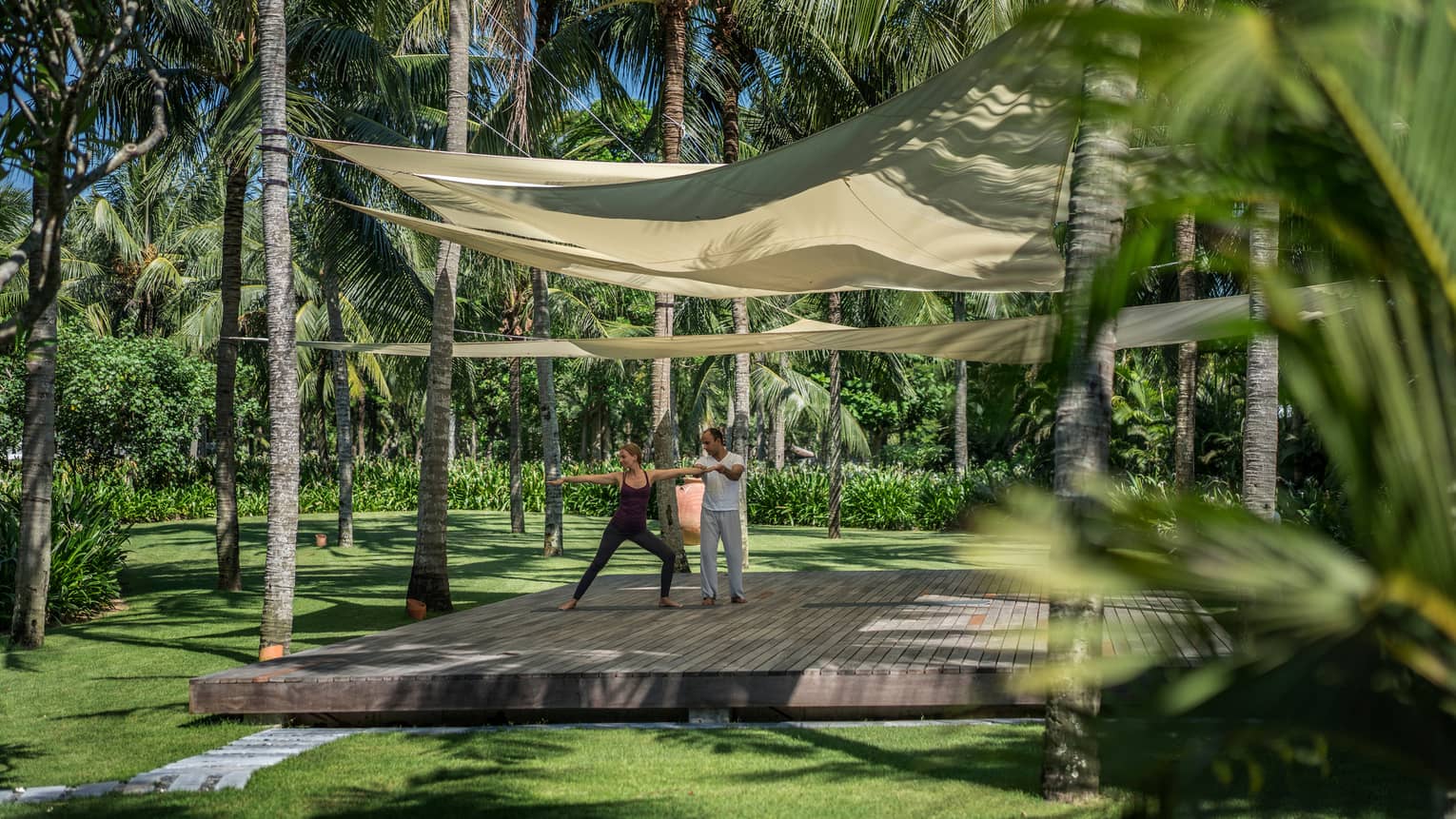 Yogi helps two people with yoga poses on wood platform under canopies