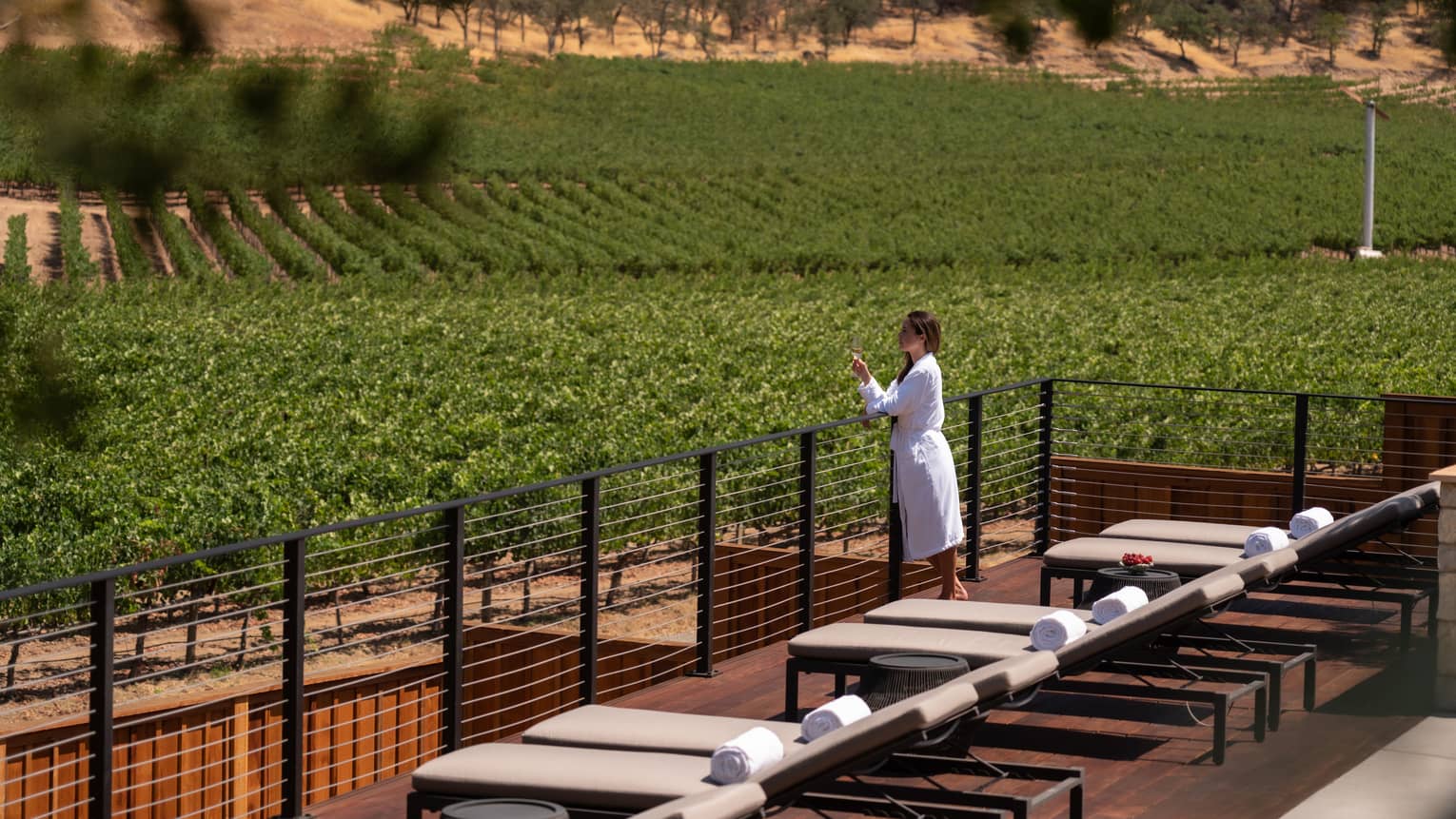 Person wearing a robe and holding a wine glass while admiring the views from the Spa sun deck.