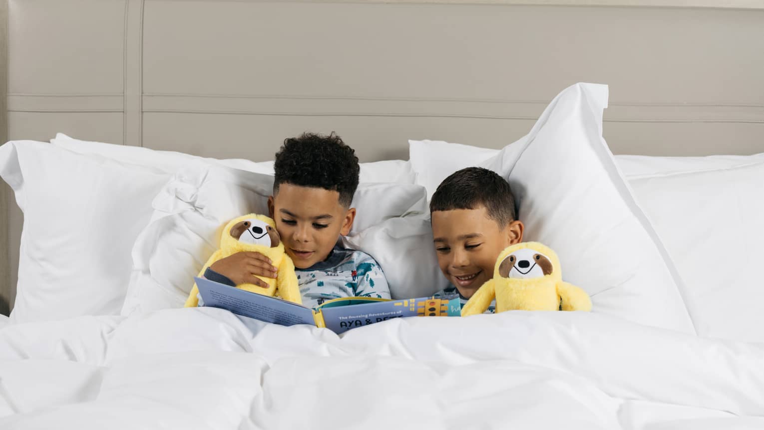Two children laying in bed with stuffed animals and a book.
