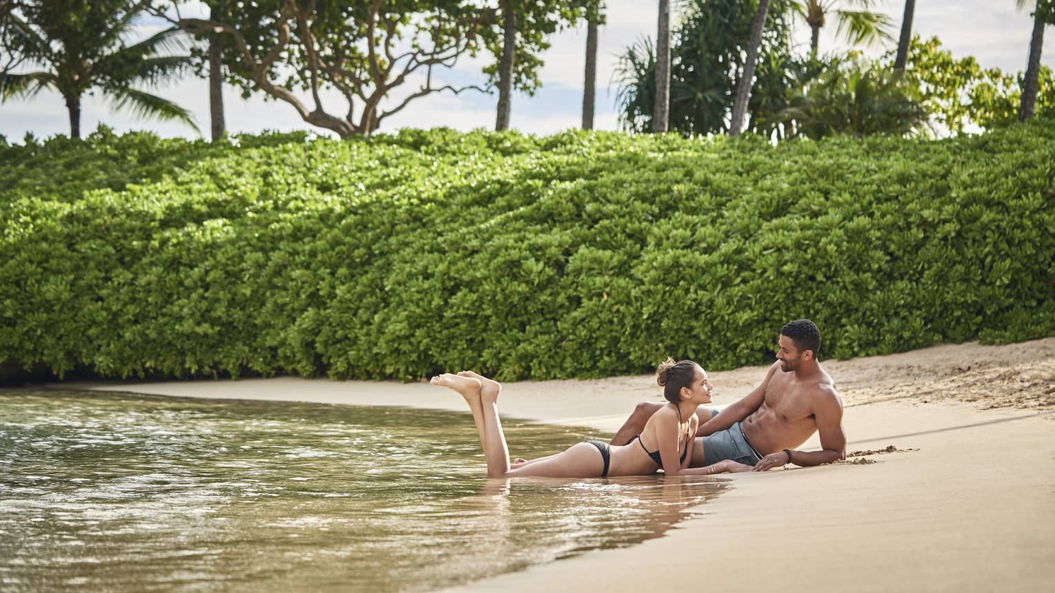Couple lounges together on the sand by the edge of the water