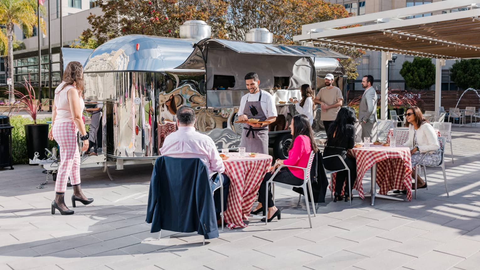 Outdoor venue with tables with red table cloths and the chef visiting a table.