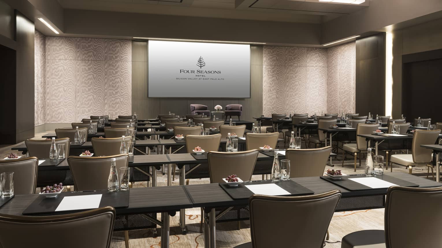 Ballroom conference with rows of meeting tables, chairs facing large screen