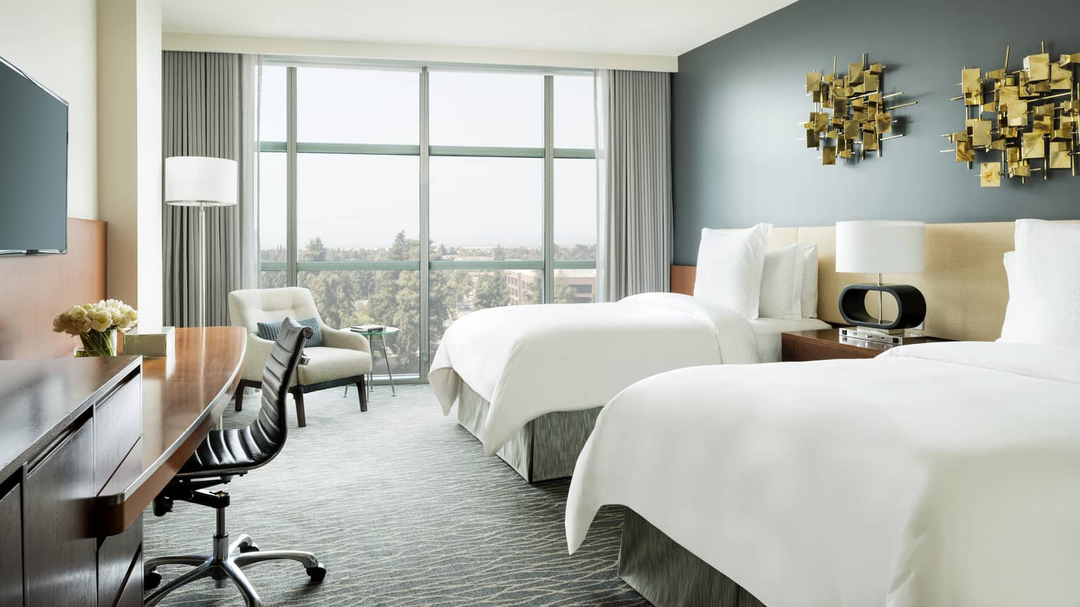 Deluxe Room double beds under modern gold art, desk under TV, armchair by window
