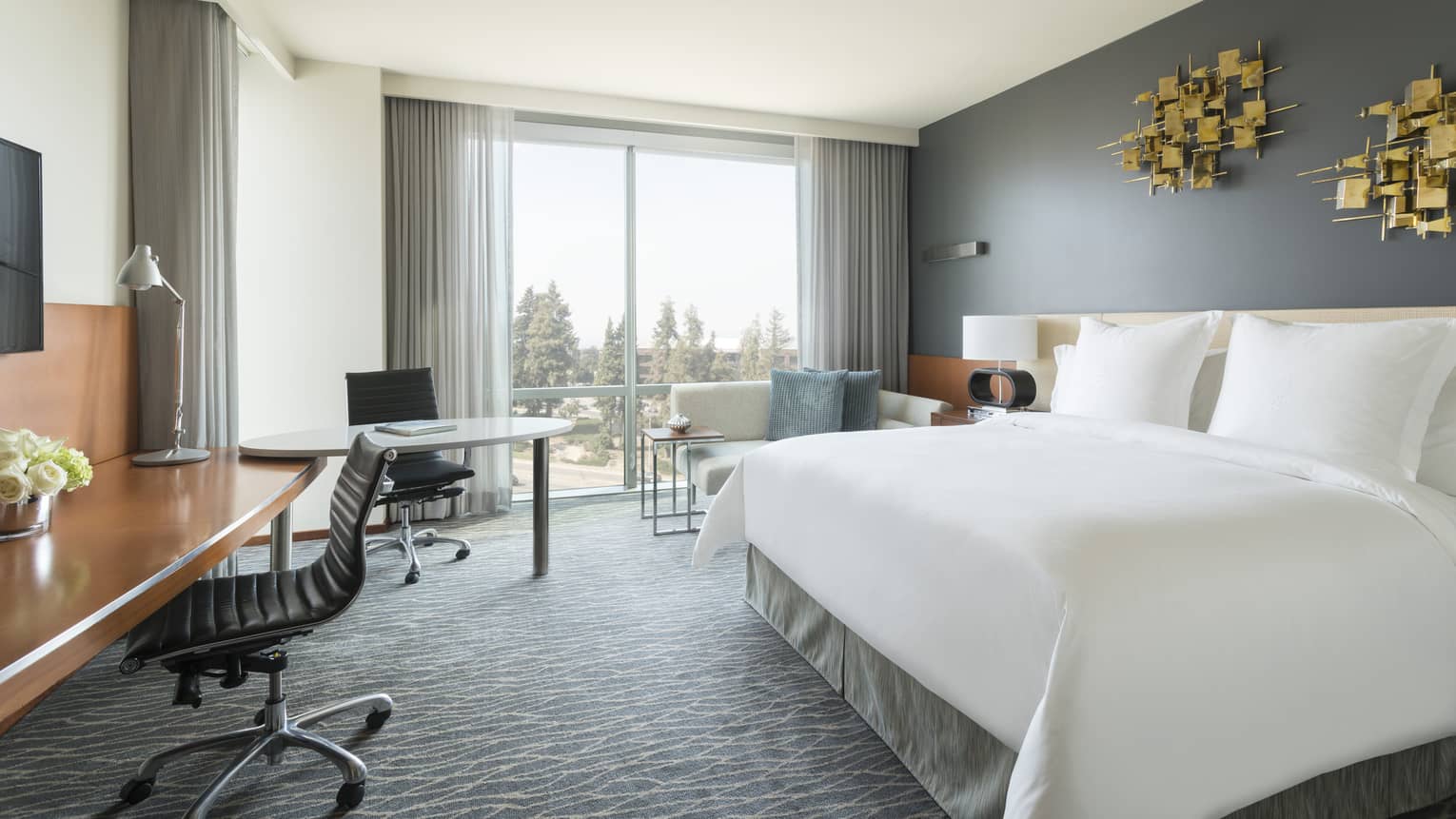 Deluxe Room bed under modern gold art, desks, chaise by window