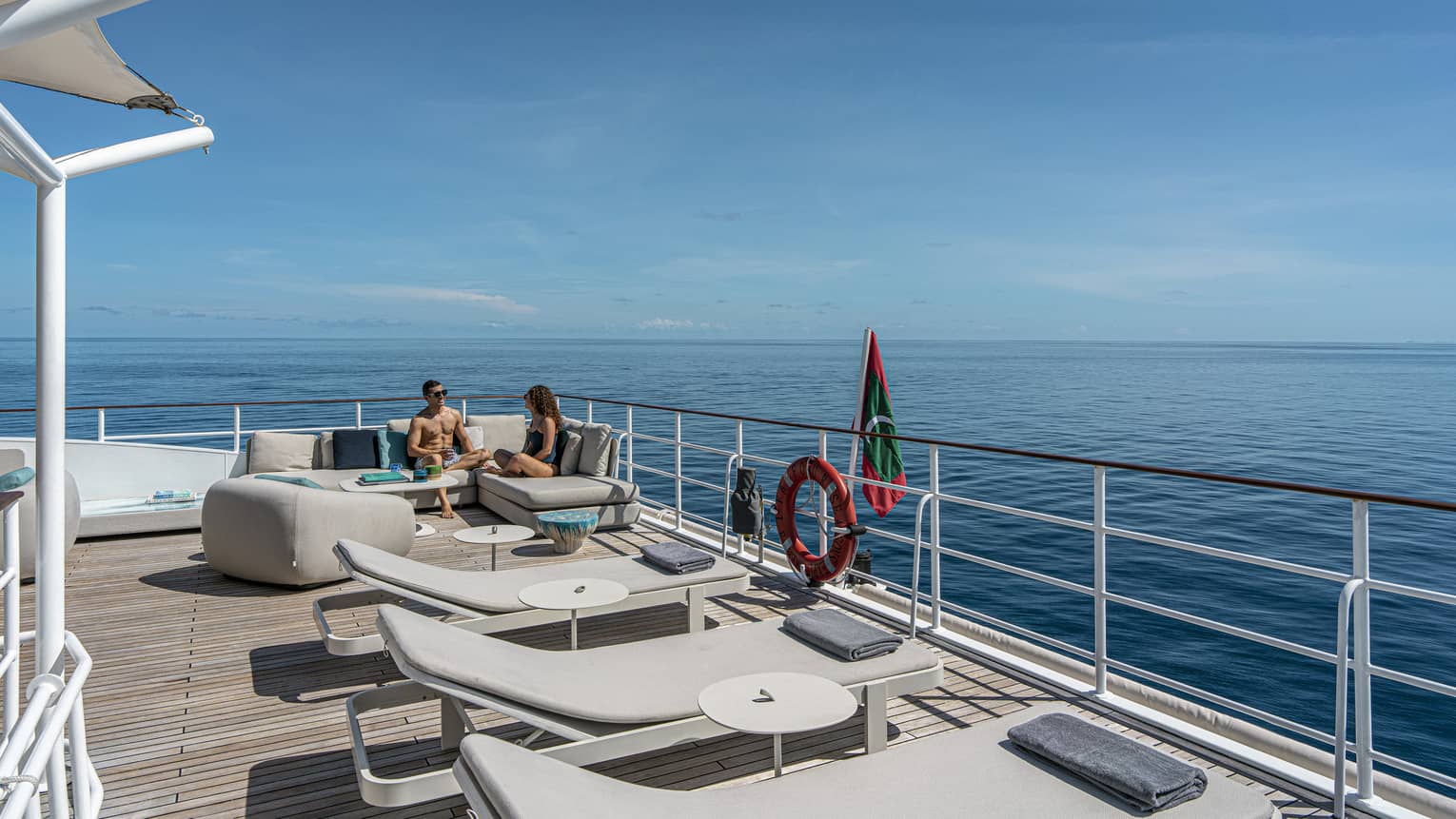 Man and woman sit in corner lounge seat on a yacht deck at sea