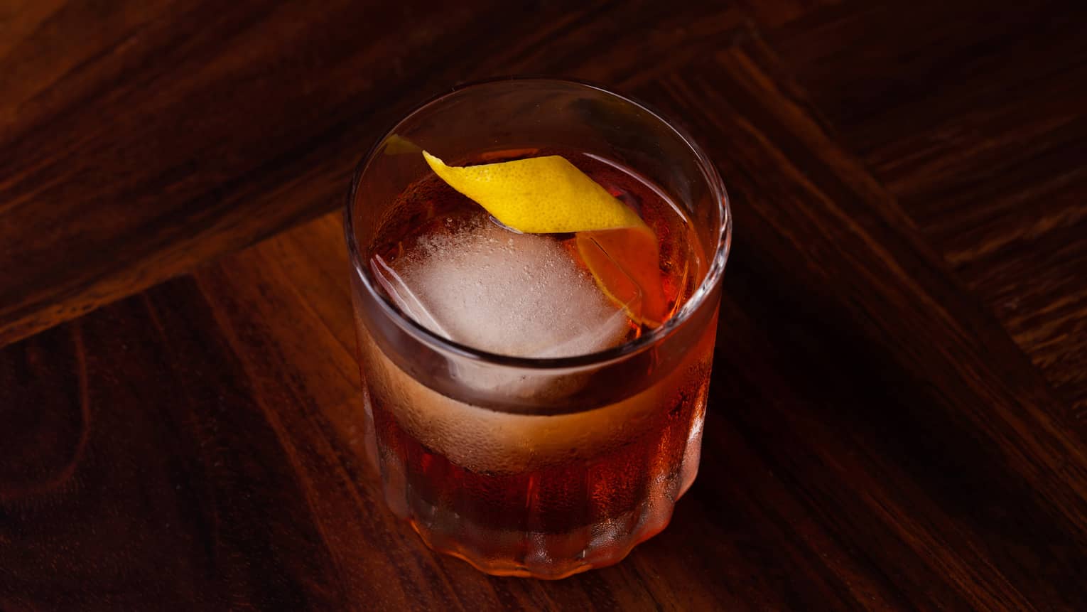 A cocktail in a small glass with an orange peel in it.