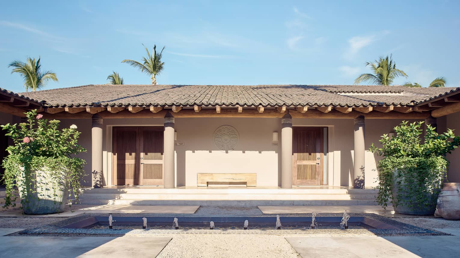 Arena Beach House exterior with shingled roof and stucco columns, large potted planted on either side of doorway