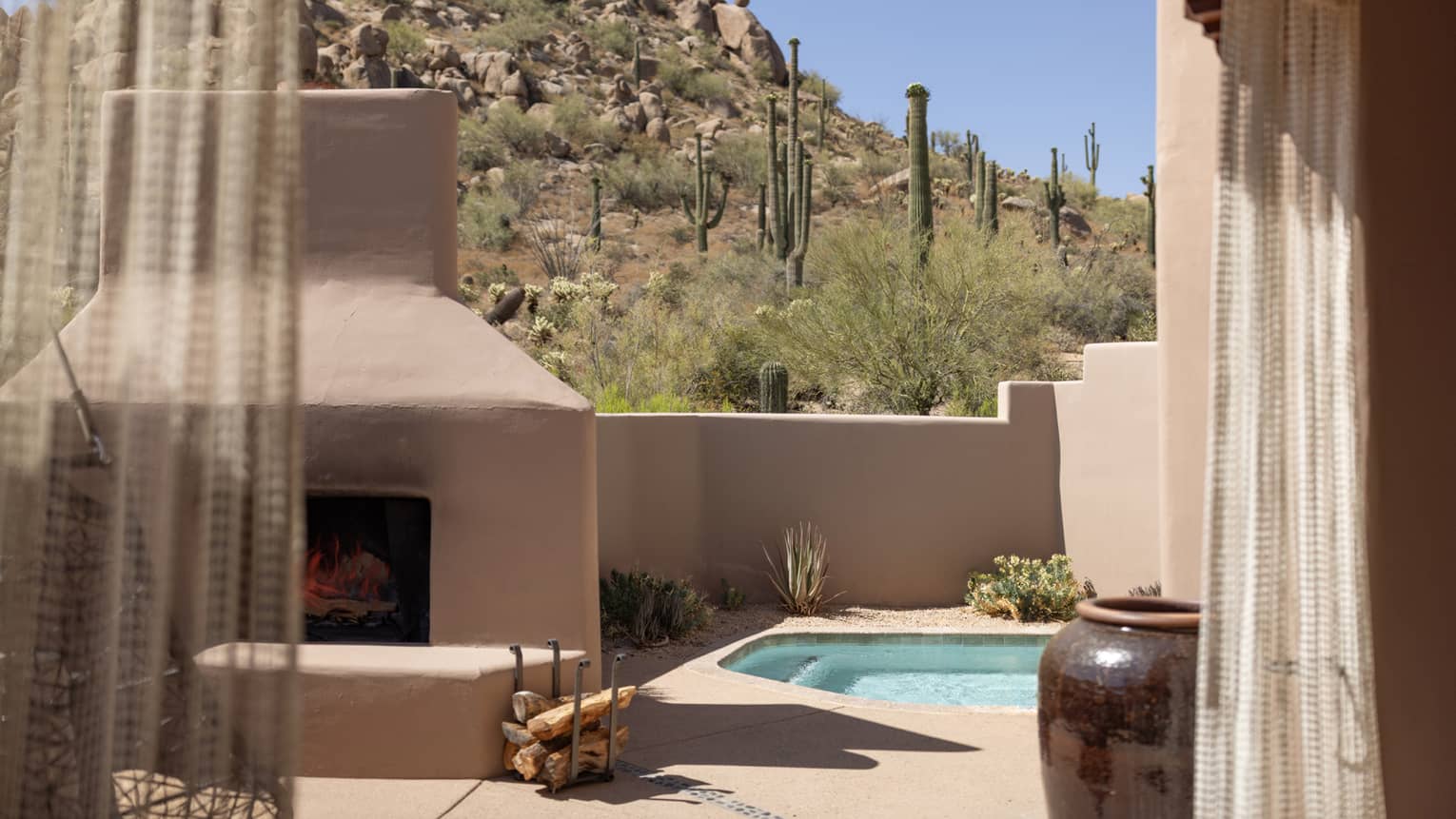 An outdoor courtyard with a plunge pool and fire near a small mountain.