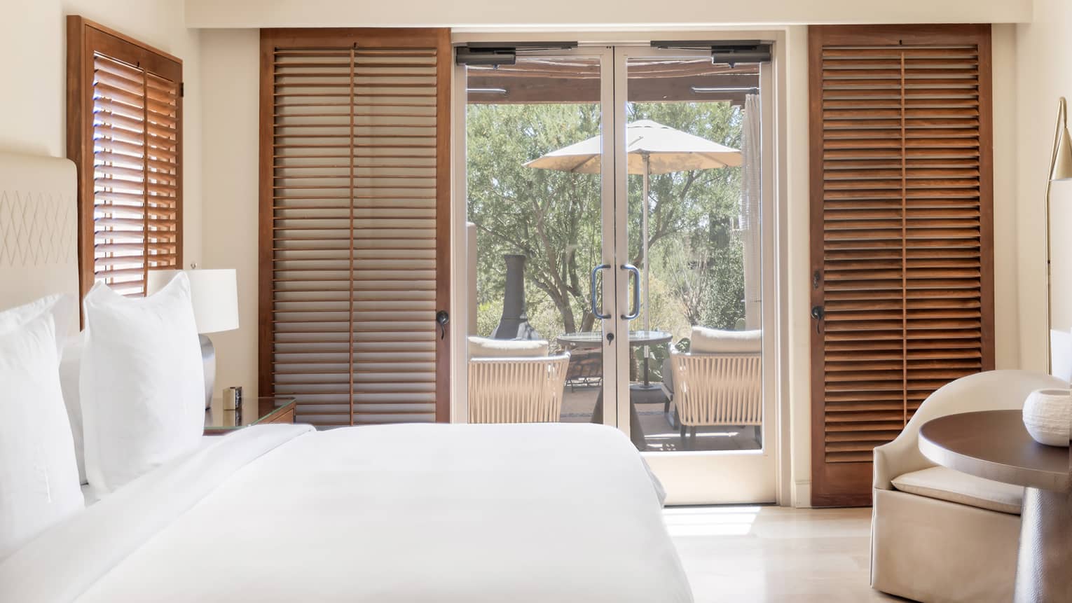 A room with a bed, chair and table, and large glass doors leading outside.