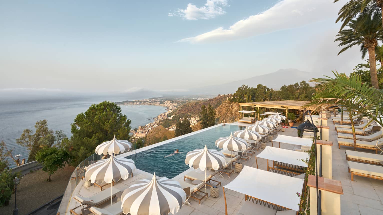 A woman swimming in an infinity pool surrounded by chic lounge sets and ocean views