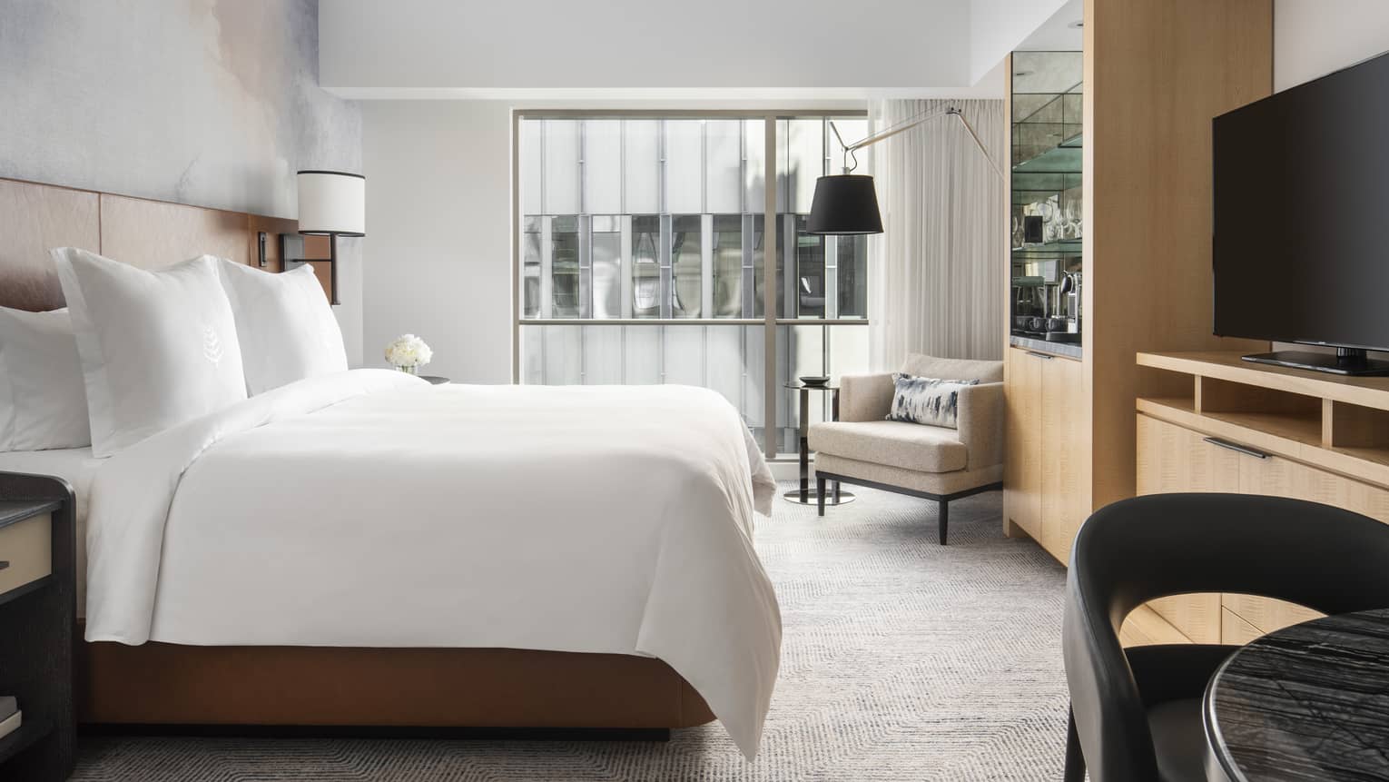 A bright bedroom as a large television, coffeemaker and cushioned chairs